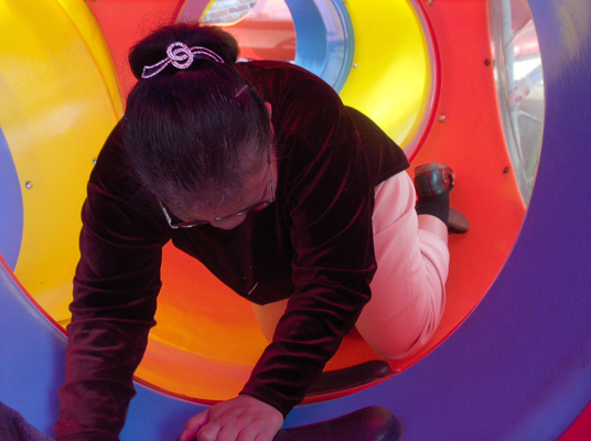 6 photos show Nanta inside colorful round tubes, crawling on her hands and knees.  When she reaches the tubular slide, she turns around and puts her feet into the slide and goes down, laughing.